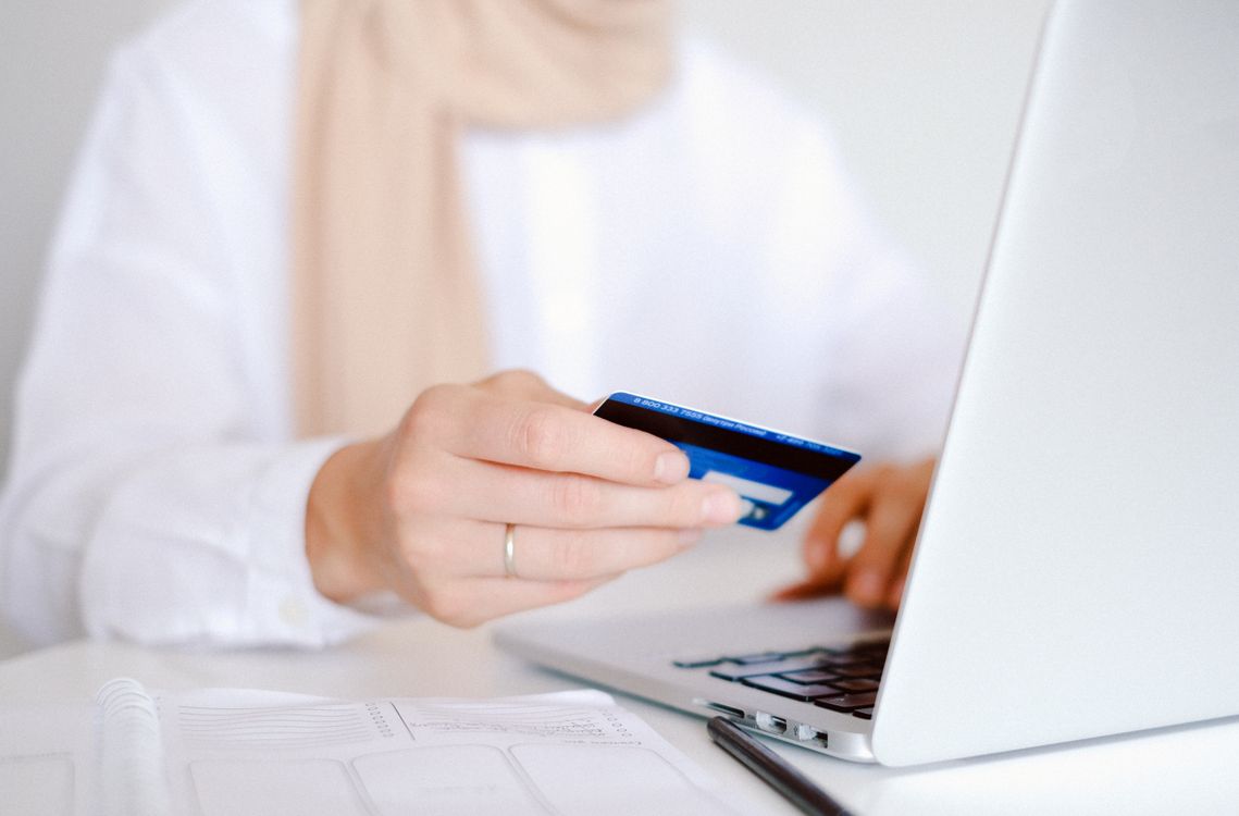 Person hält Kreditkarte vor geöffnetem Laptop