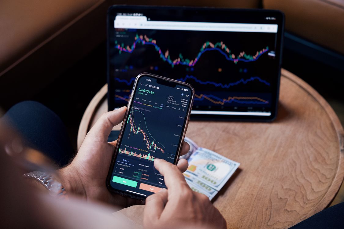 Person prüft Trading-Charts auf Smartphone und Tablet