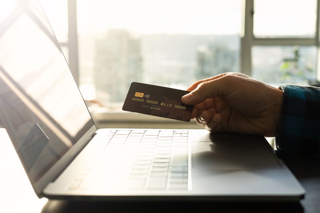 Person hält eine Kreditkarte vor einem geöffneten Laptop, symbolisiert Online-Vergleichsportale
