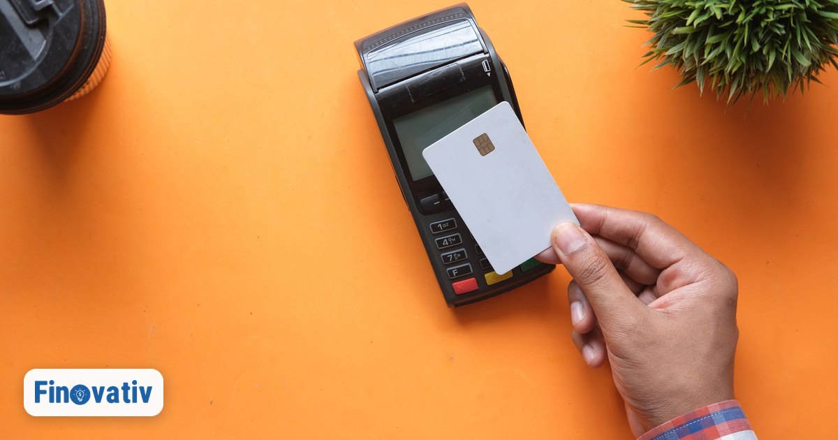 Hand hält eine weiße Kreditkarte an ein Bezahlterminal auf orangefarbenem Untergrund